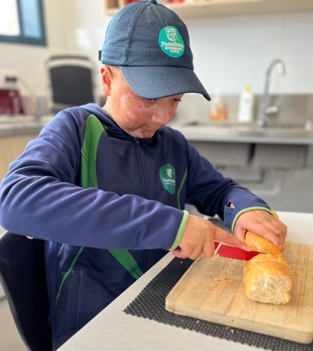 Akonga sitting at a table using a knife to slice a bread stick