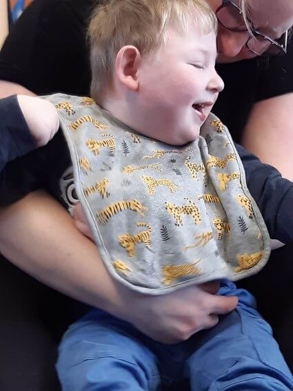 Child is sitting on parent's knee enjoying music and movement via zoom session.