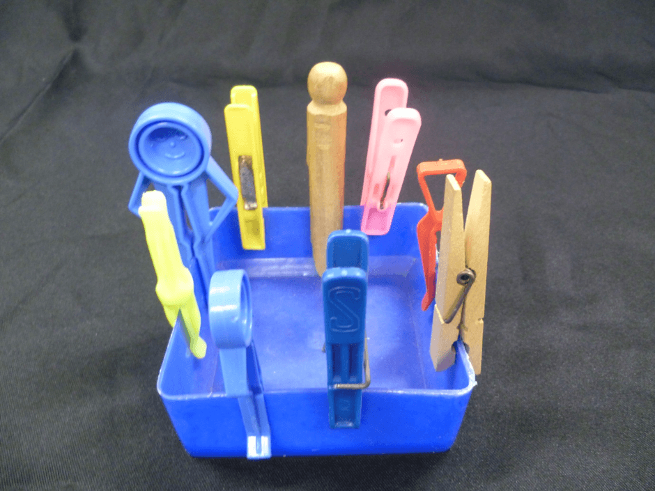nine clothes pegs of different types pegged to the side of an ice cream container, wooden or plastic push or spring loaded action.