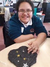 Te Ngaru is sitting at a table with her finger on her dough which has the 7 sister glitter stars in it.